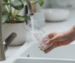 Woman filling glass with water from tap in kitchen, closeup